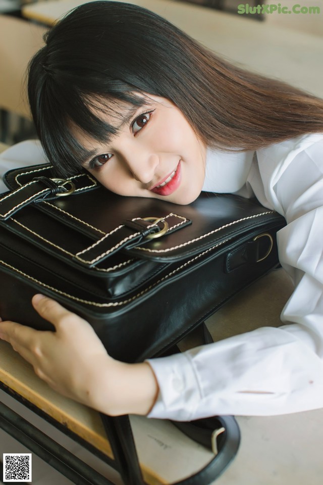 A woman in a white shirt holding a black purse.