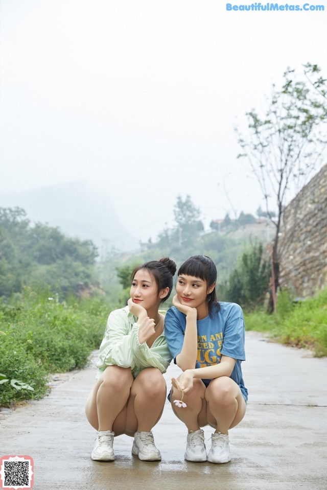 Two young women sitting on the side of a road.