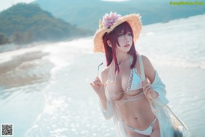 A woman in a bikini and a straw hat on the beach.