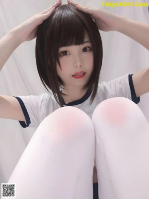 A woman in white stockings and a white shirt is sitting on a bed.