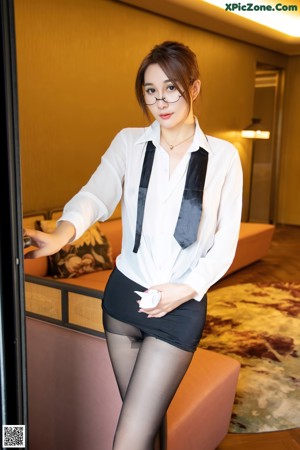 A woman in a white shirt and black skirt sitting on a couch.