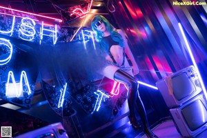 A woman sitting on a red chair in front of a neon sign.