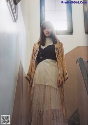 A woman with long brown hair wearing a beige jacket.