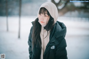 A woman standing in the snow wearing a black coat.