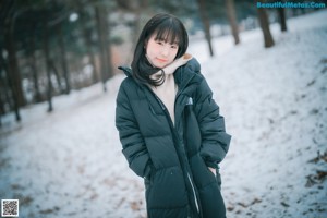 A woman crouching down in the snow holding a handful of snow.