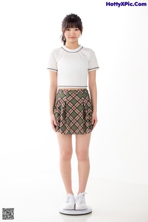 A young woman in a white shirt and plaid skirt posing for a picture.