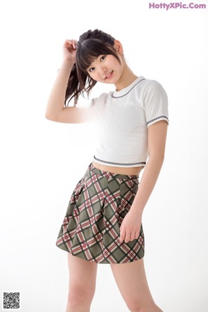 A woman in a white shirt and plaid skirt posing for a picture.