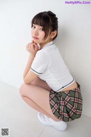 A woman in a white shirt and plaid skirt posing for a picture.