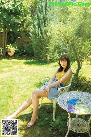 A woman sitting on a white chair in a garden.