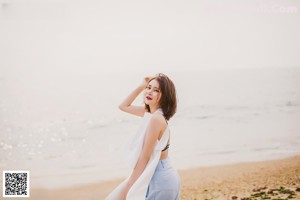 A woman in a white top and blue pants on the beach.