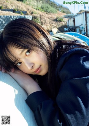 A young woman leaning against a wall with her hand on her chin.