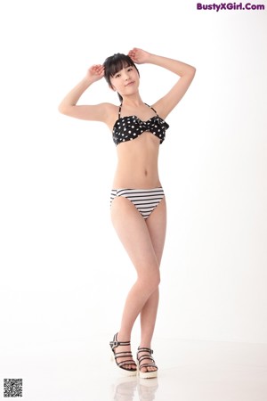 A woman in a black and white bikini leaning against a wall.