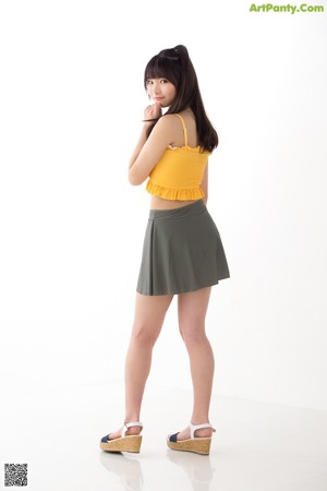 A woman in a yellow top and green skirt posing for a picture.