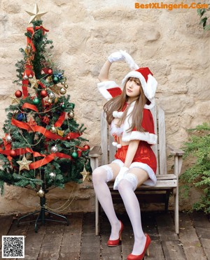 A woman in a santa claus outfit standing next to a Christmas tree.